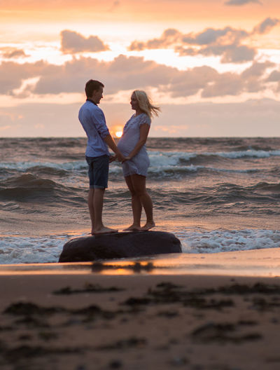 Side view of expectant couple standing on shore at beach during sunset