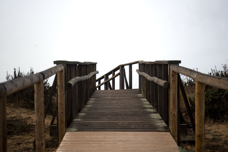 Wooden footbridge on pier against clear sky