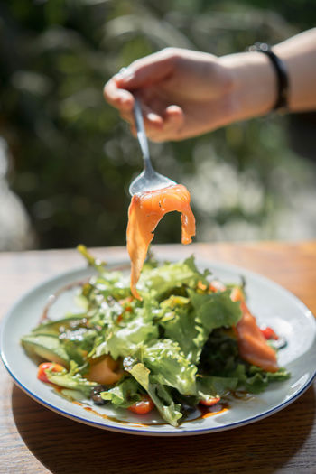 Cropped hand holding salad with spoon served on table