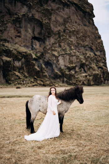 Woman with horse standing on field against rock formation