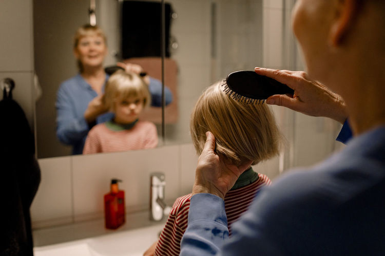 Grandmother combing hair of grandson in bathroom at home