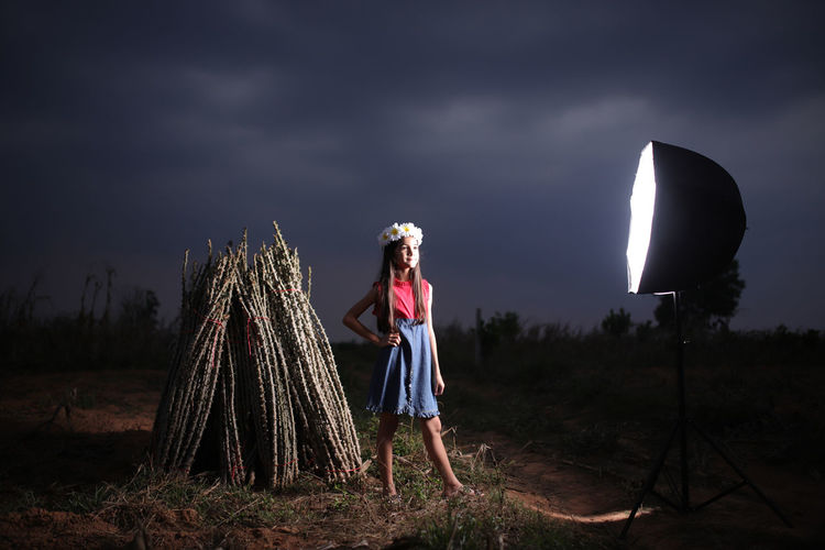 Cute girl standing by illuminated lighting equipment on field against sky at night