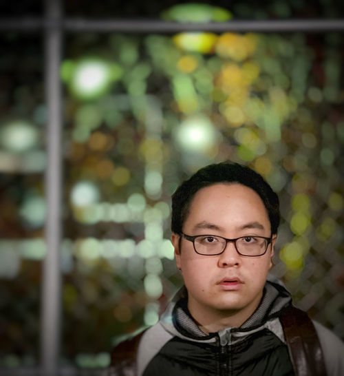 Portrait of a young man wearing eyeglasses against street and neon lights at night