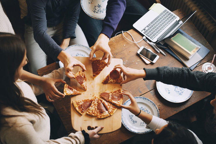 High angle view of friends taking slices of pizza at dining table