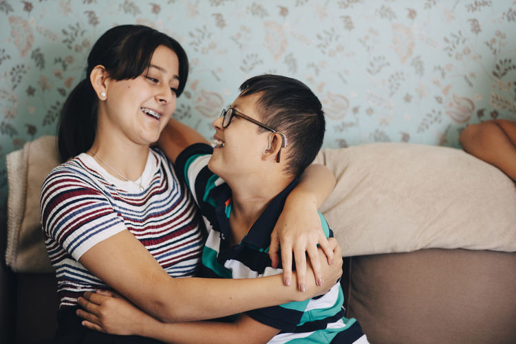 Loving brother and sister embracing on sofa against wall in living room