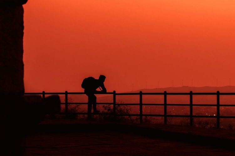 Silhouette man standing by railing against hill view during sunset
