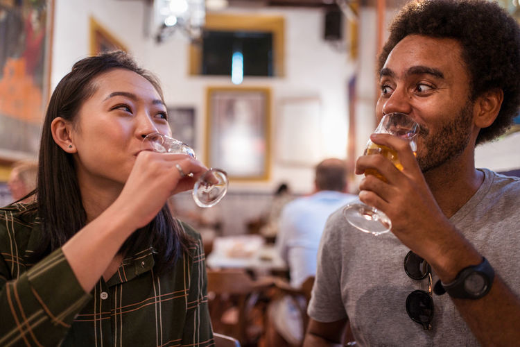 Soft focus of multiracial couple drinking beverages while having dinner together in modern restaurant during festive event