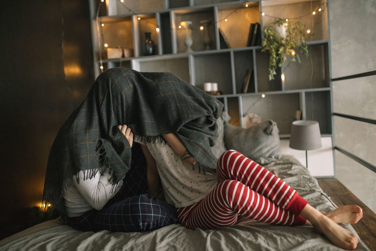 Couple with blanket on face sitting in bed at home