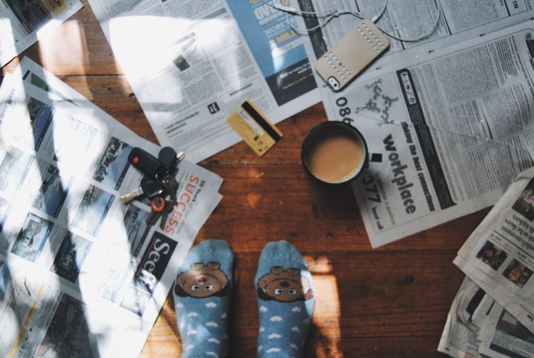 Low section of person in socks by tea amidst newspapers on floorboard