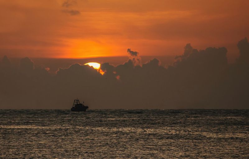 Silhouette boat sailing in sea against sky during sunset