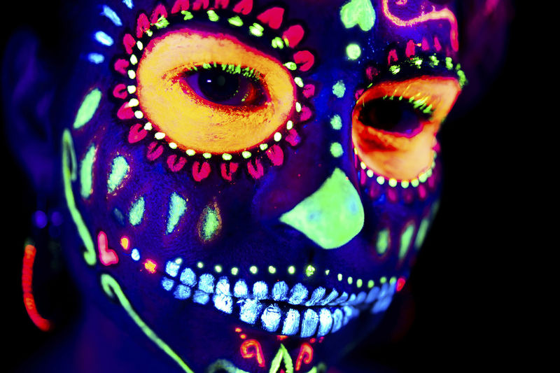 Anonymous female in multicolored masquerade mask with flowers on head looking at camera on halloween night