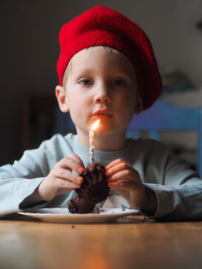 Portrait of cute little boy holding birthday cake with a burning candle.