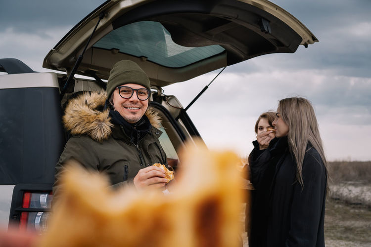 Man and friends eating pizza by car on the beach  in winter