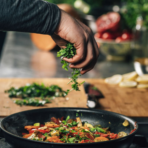 Hand adding parsley into frying pan with vegetables