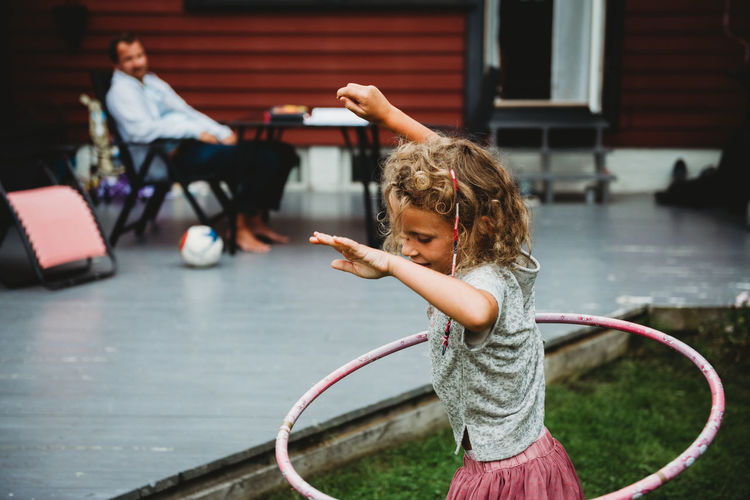 Side view of cute girl playing with hula hoop in summer in backyard