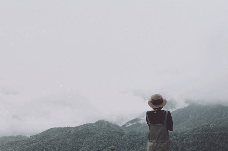 Rear view of woman looking at mountains against cloudy sky