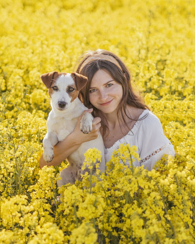 Beautiful woman with dog amidst yellow flowers on field