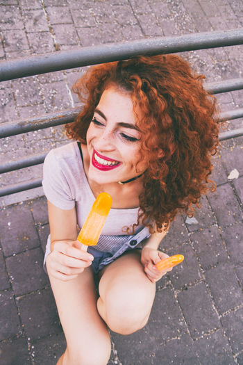 High angle view of happy woman having orange popsicles on footpath