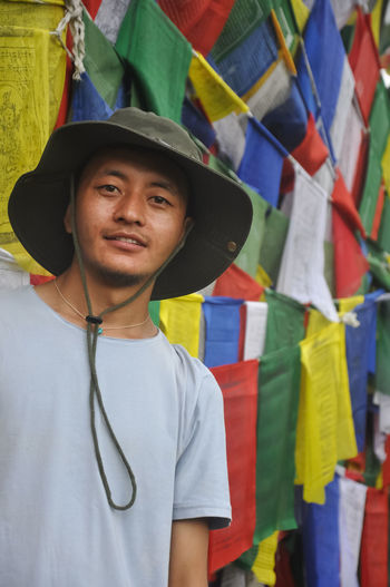 A asian young guy looking at camera, standing against buddhist prayer flags