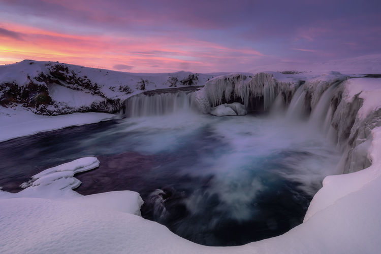 Scenic view godafoss falls on snowcapped mountains against sky during sunset