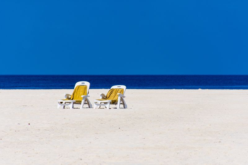 Deck chairs at beach against clear blue sky