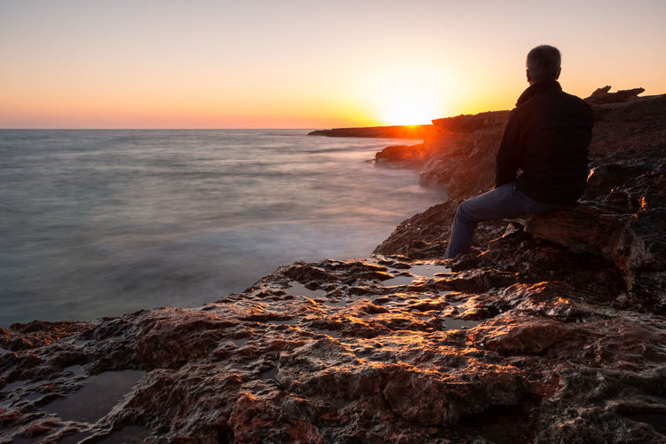 Man sitting on the rocks by the sea watching the sunset. long exposure
