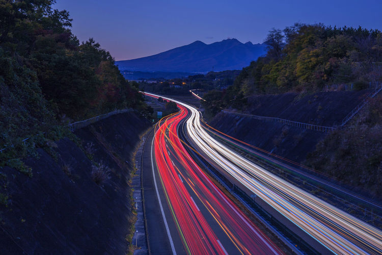 Light trails on road by mountain against sky at night