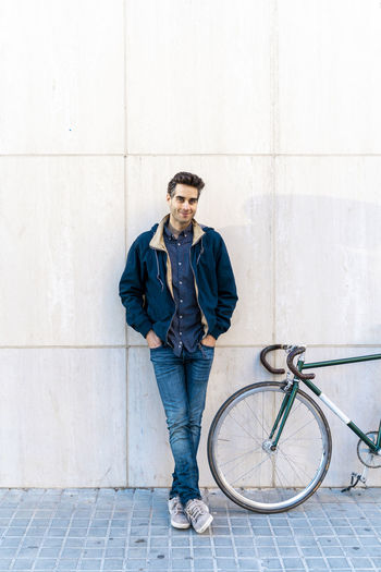 Portrait of casual man with bicycle standing at a wall