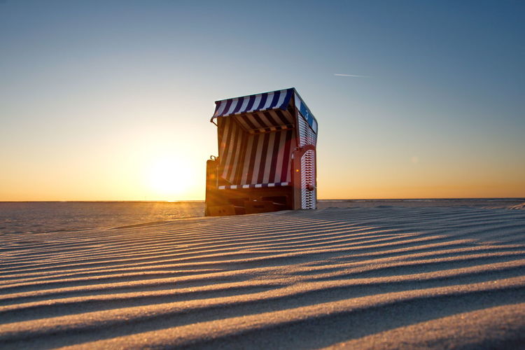Lifeguard hut on beach against clear sky during sunset