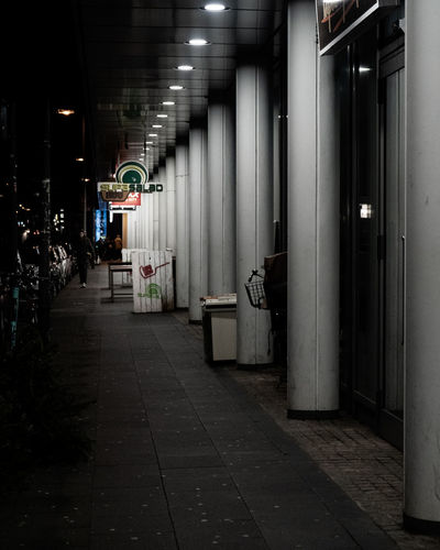 Illuminated street lights on footpath amidst buildings in city at night