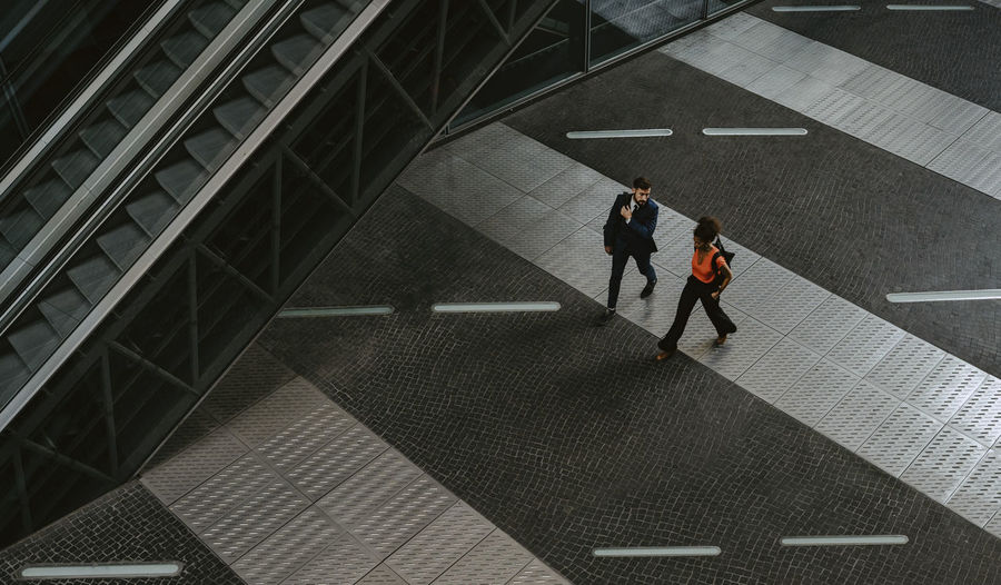 Male and female colleagues discussing while walking by escalator on walkway