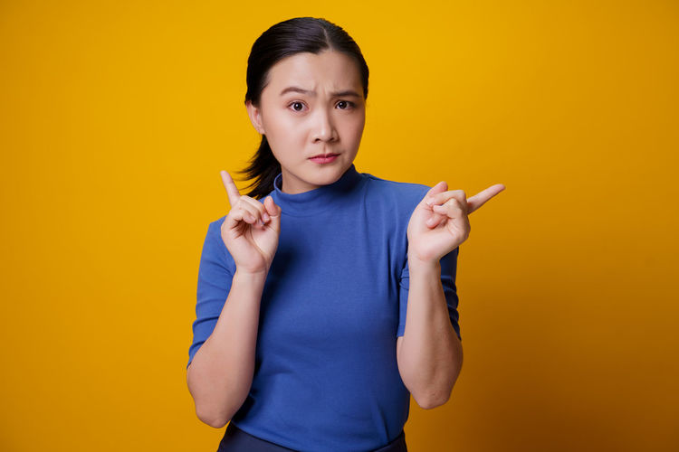Portrait of young woman holding cigarette against yellow background