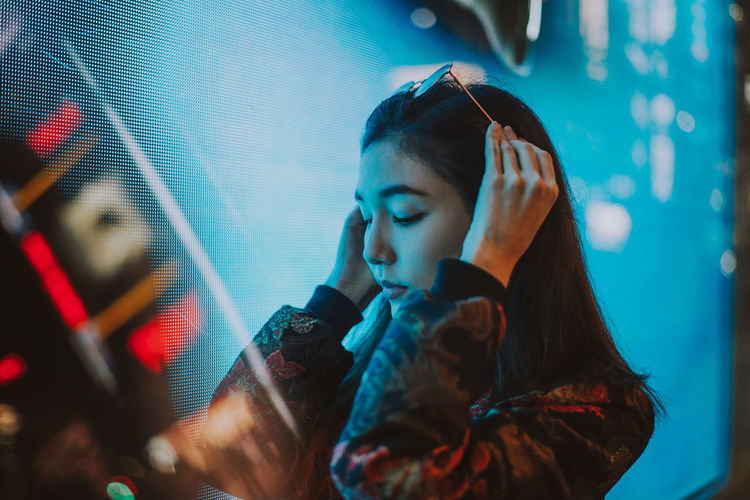 Close-up of young woman standing against illuminated city at night