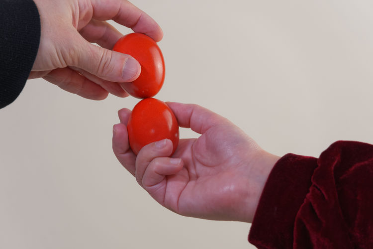 Cropped hands of people holding red eggs against white background