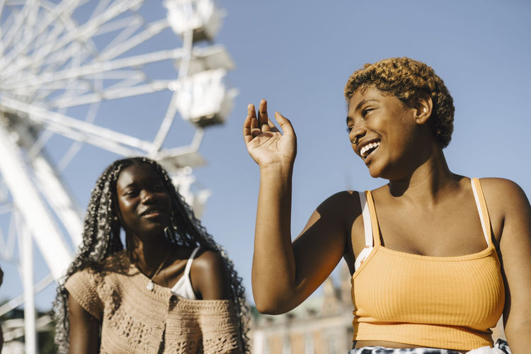 Young woman looking at happy friend against ferris wheel on sunny day
