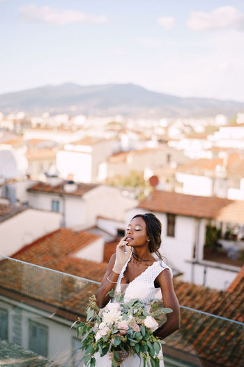 Bride holding flowers standing against cityscape