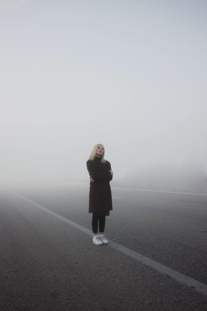 WOMAN STANDING ON ROAD IN FOGGY WEATHER