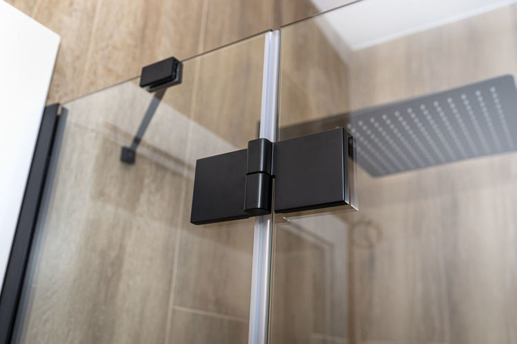 Black matt hinge connecting the wings of the shower enclosure flush with the glass, view  outside.