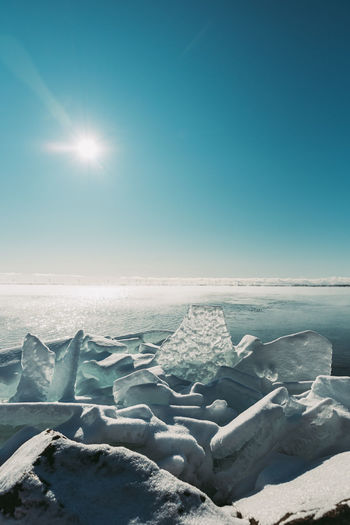 Large flat pieces of ice piled up along the shore of a lake in winter.