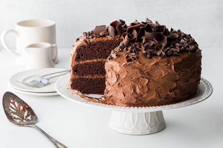 A triple layered chocolate cake with slices removed, against a light background.