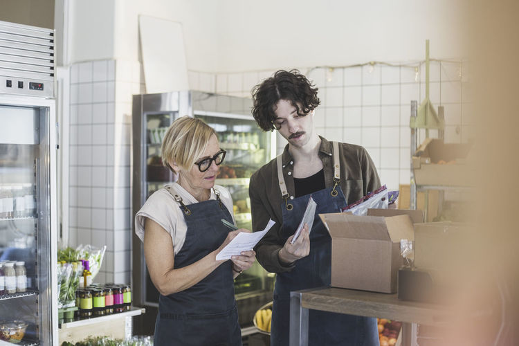 Female entrepreneur making notes while male employee showing package food in store
