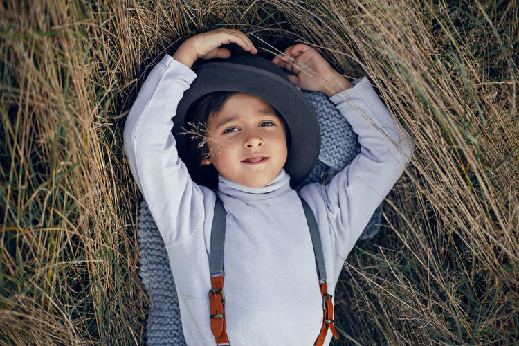 Boy child in plaid pants, hat, suspenders and scarf stands in a field in autumn
