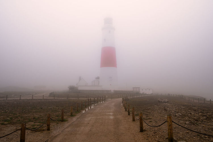 Lighthouse amidst buildings against sky during foggy weather