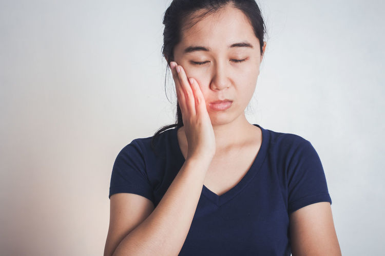 Young woman suffering from toothache while standing against white background