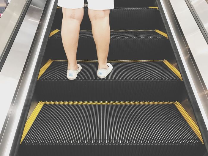 Low section of person standing on escalator at subway station