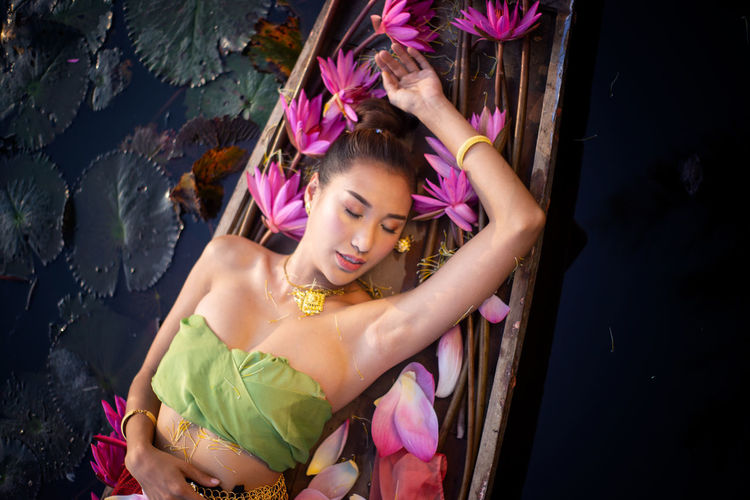 High angle view of young woman lying by pink lotus on boat in lake