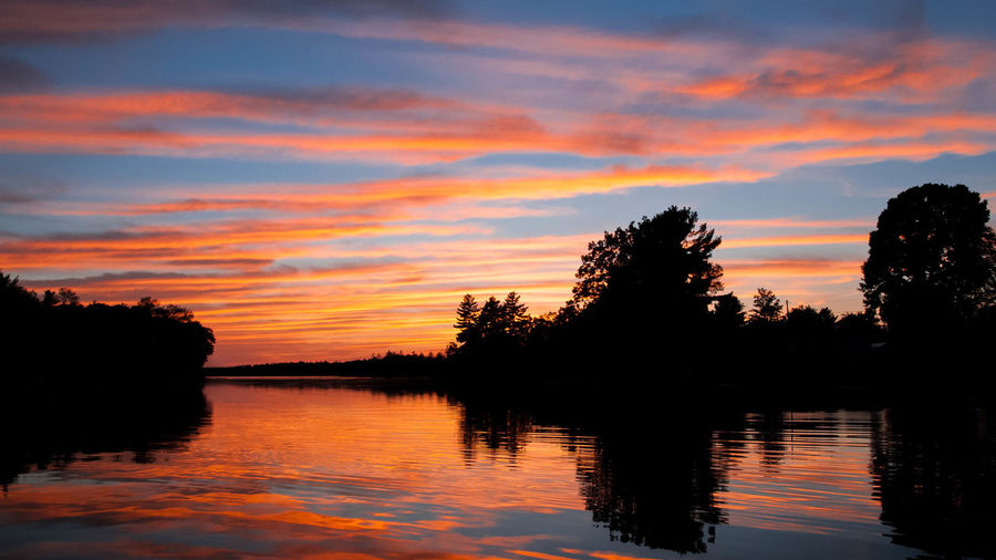 Silhouette trees by lake against romantic sky at sunset