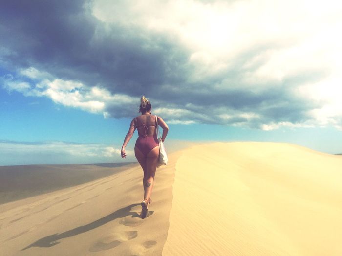 Rear view full length of woman in bikini walking at sandy beach against sky