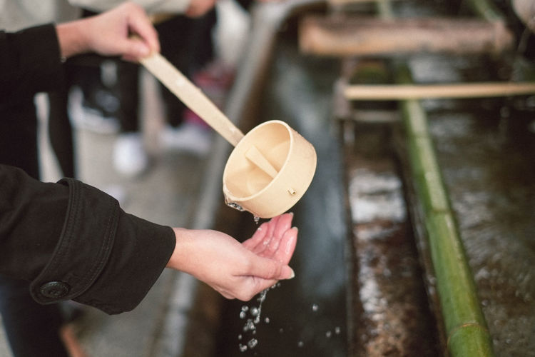Cropped image of woman washing hand while pouring water from wooden spoon