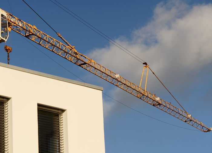 Crane boom in front of a bright blue sky above the corner of a new building, abstract